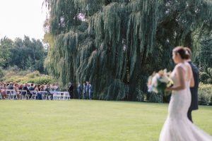 Outdoor winery wedding ceremony on a lawn beneath a willow tree at Aurora Cellars, Lake Leelanau, MI